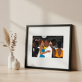 Framed artwork of a couple embracing at a party on a wooden surface with decorative vases.