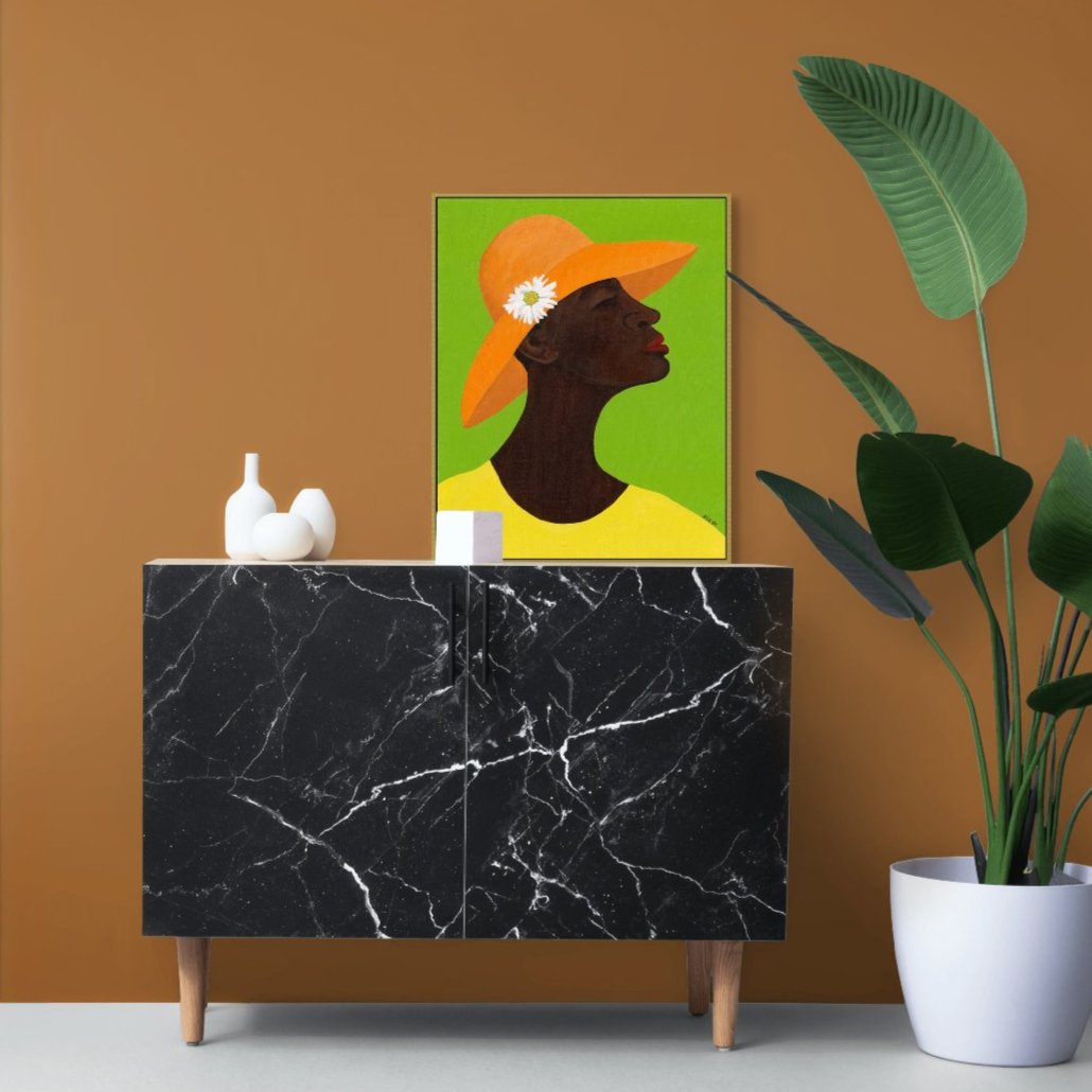 'Annabelle's New Hat' framed stretched canvas giclee art print: African American woman in yellow attire, orange hat with daisy, against green, placed on a black cabinet in a living room.