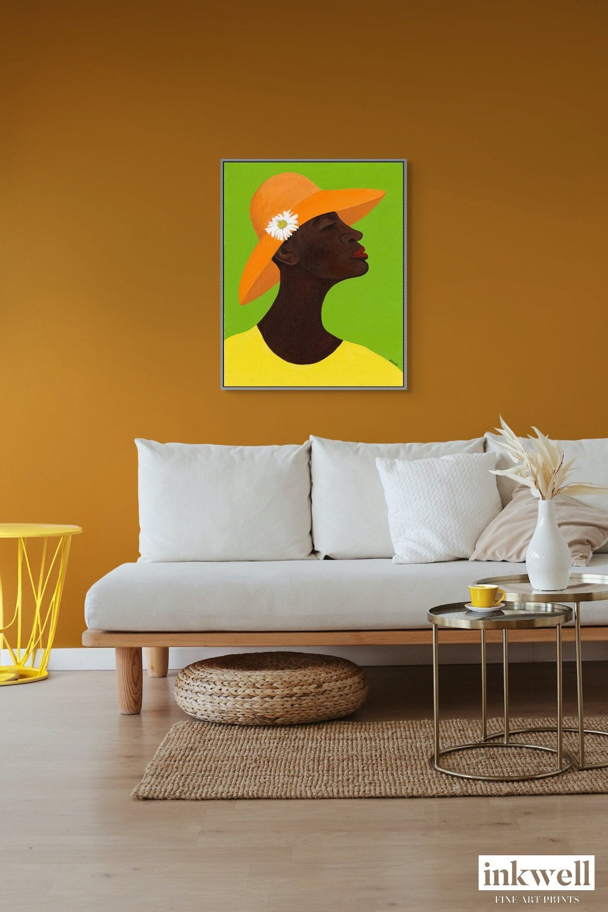 Annabelle's New Hat' giclee art print on framed stretched canvas: African American woman in yellow attire, orange hat with daisy, set against green, framed in silver wood float frame, shown above a cozy white sofa.