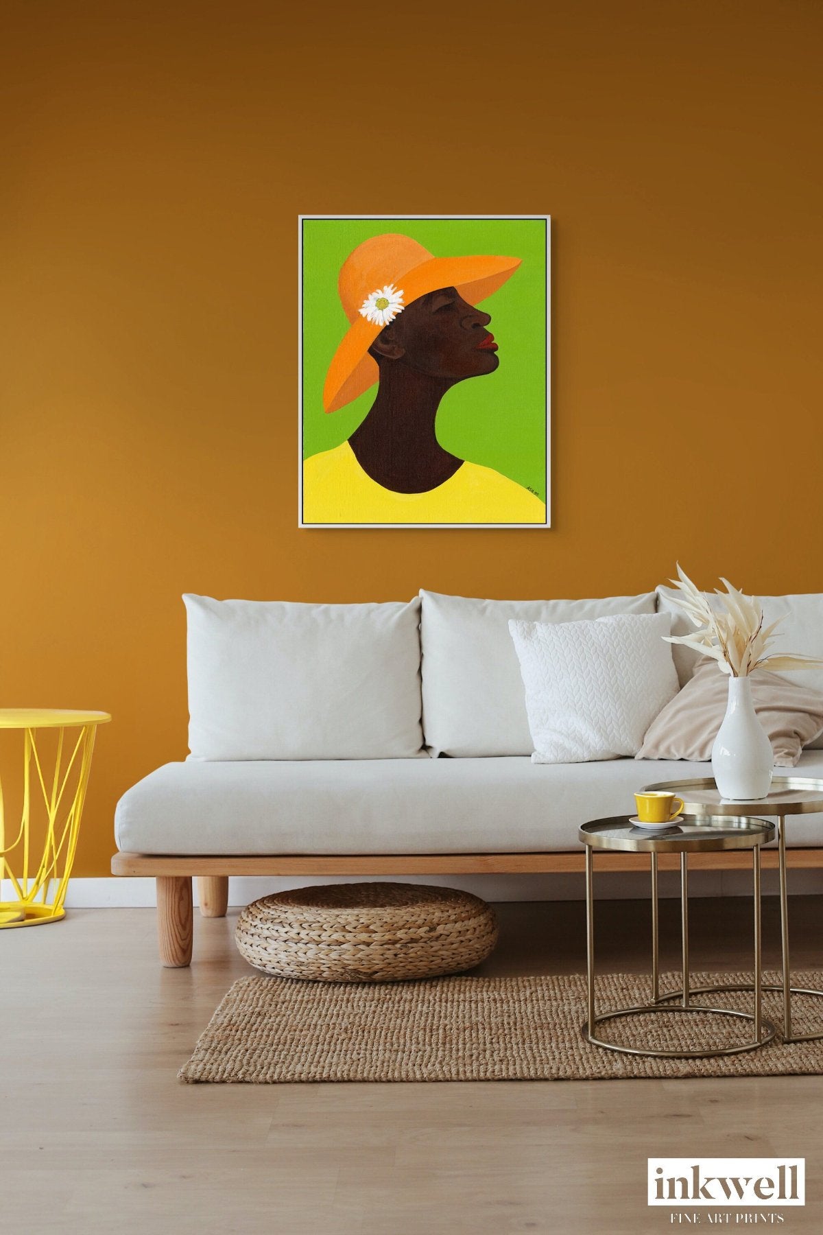 Annabelle's New Hat' giclee art print on framed stretched canvas: African American woman in yellow attire, orange hat with daisy, set against green, framed in white wood float frame, shown above a cozy white sofa.