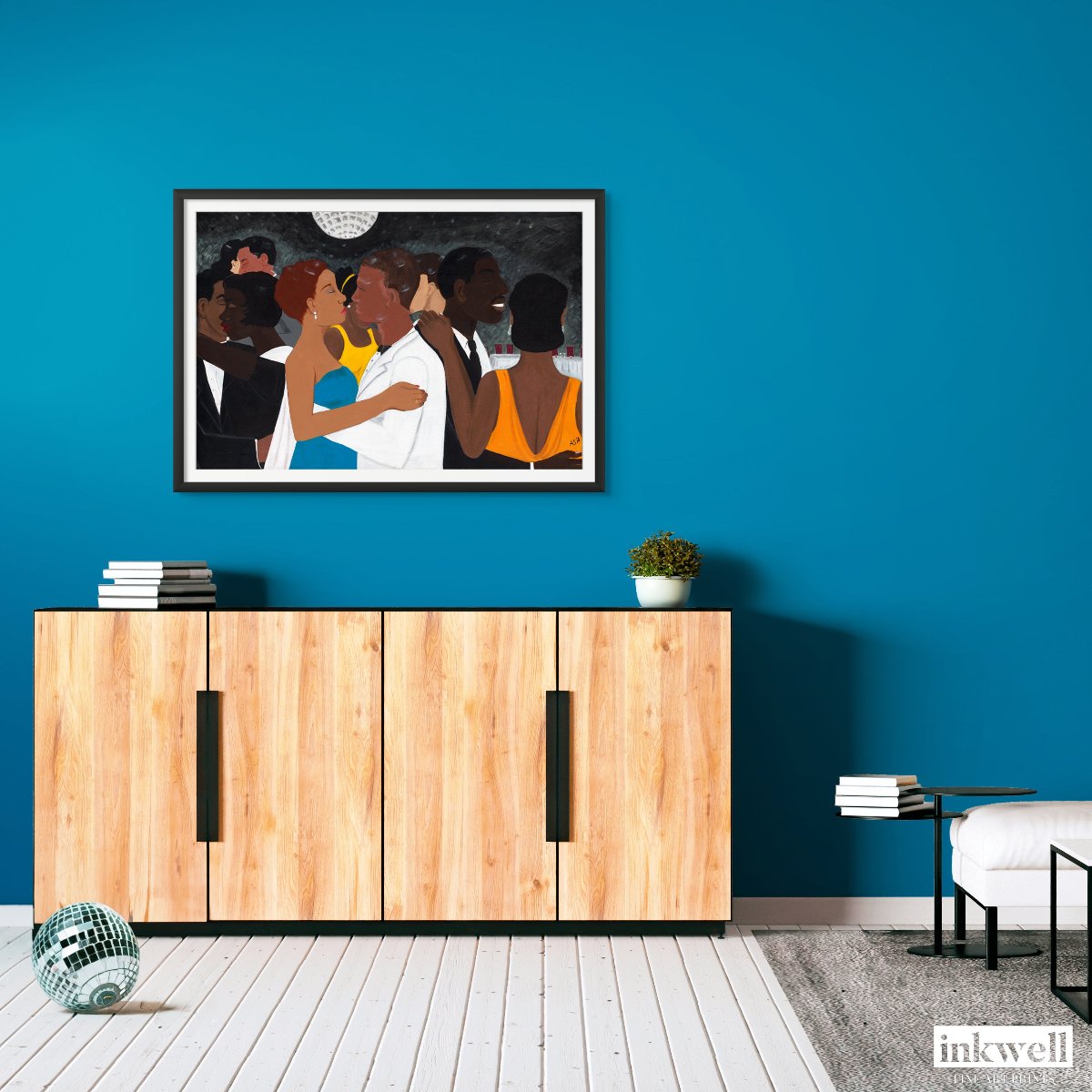 'Black Tie Affair' fine art print: Couple in blue and yellow dress, white suit, amidst elegantly dressed figures against a monochromatic background, framed in black, displayed on a blue-green wall above a light wood cabinet