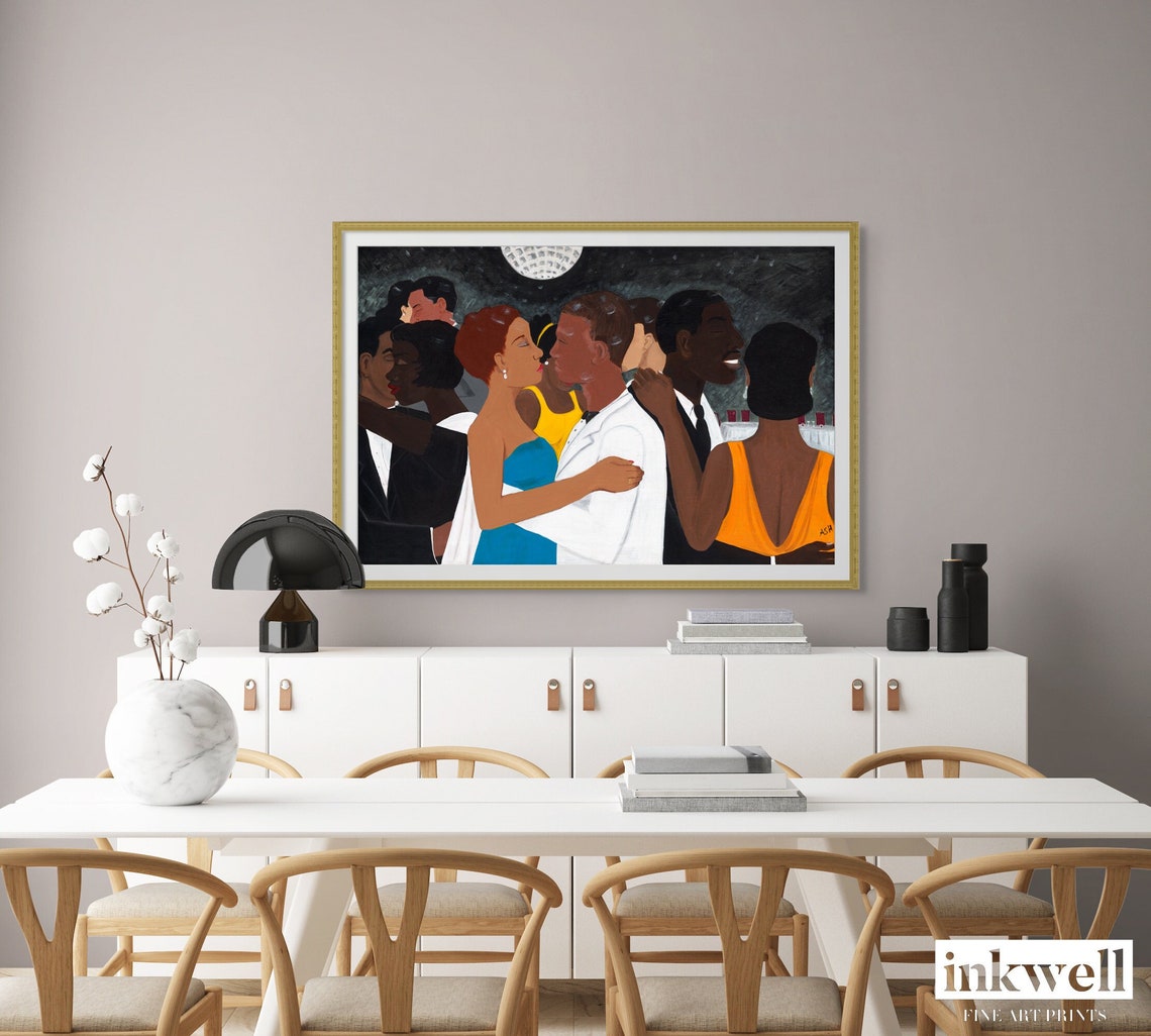 'Black Tie Affair' fine art print: Couple in blue and yellow dress, white suit, amidst elegantly dressed figures against a monochromatic background, framed in gold wood, showcased above a white cabinet in a dining room.