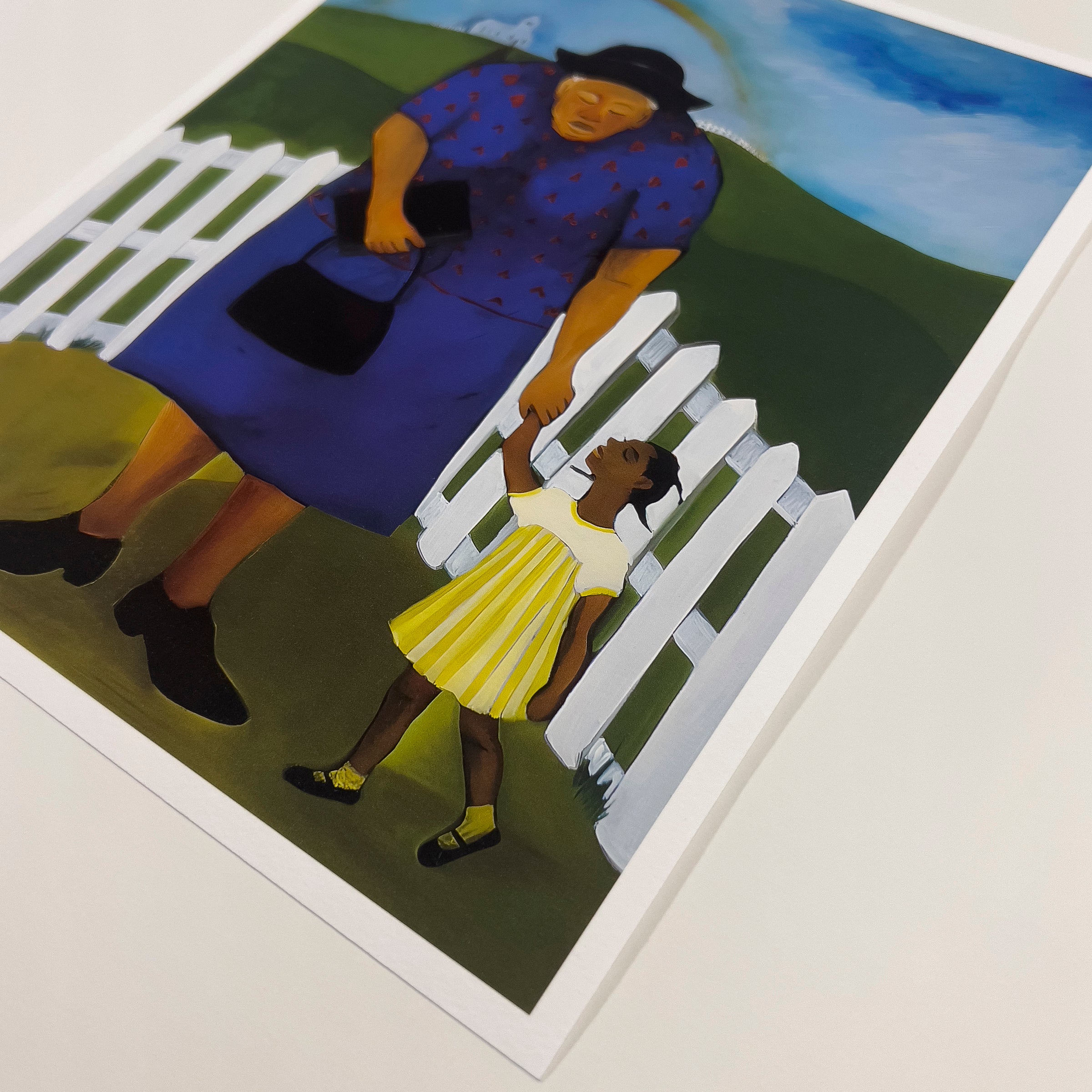 An art print showing a young Black girl in a yellow dress walking hand in hand with her elder toward a white church on a hill, beneath a bright rainbow and blue sky, surrounded by green fields and a white picket fence.