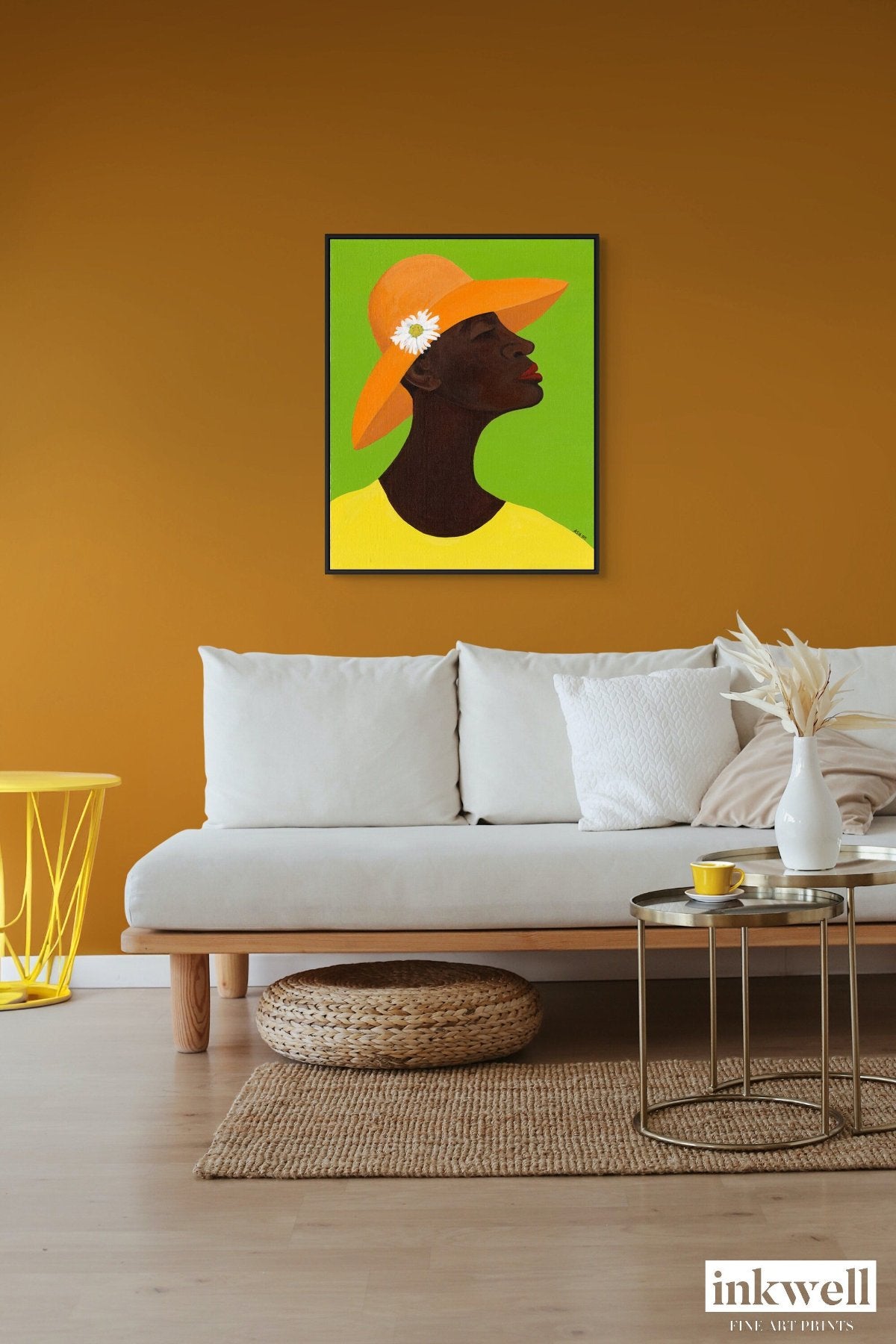 Annabelle's New Hat' giclee art print on framed stretched canvas: African American woman in yellow attire, orange hat with daisy, set against green, framed in black wood float frame, shown above a cozy white sofa.