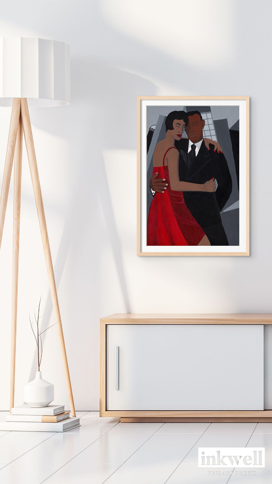 'Night on the Town' art print: Elegantly dressed couple, woman in a red dress and man in a black suit, embracing against a stylized urban backdrop with abstract buildings, capturing a romantic and celebratory evening atmosphere. hung on a white wall above a media cabinet, framed in natural wood