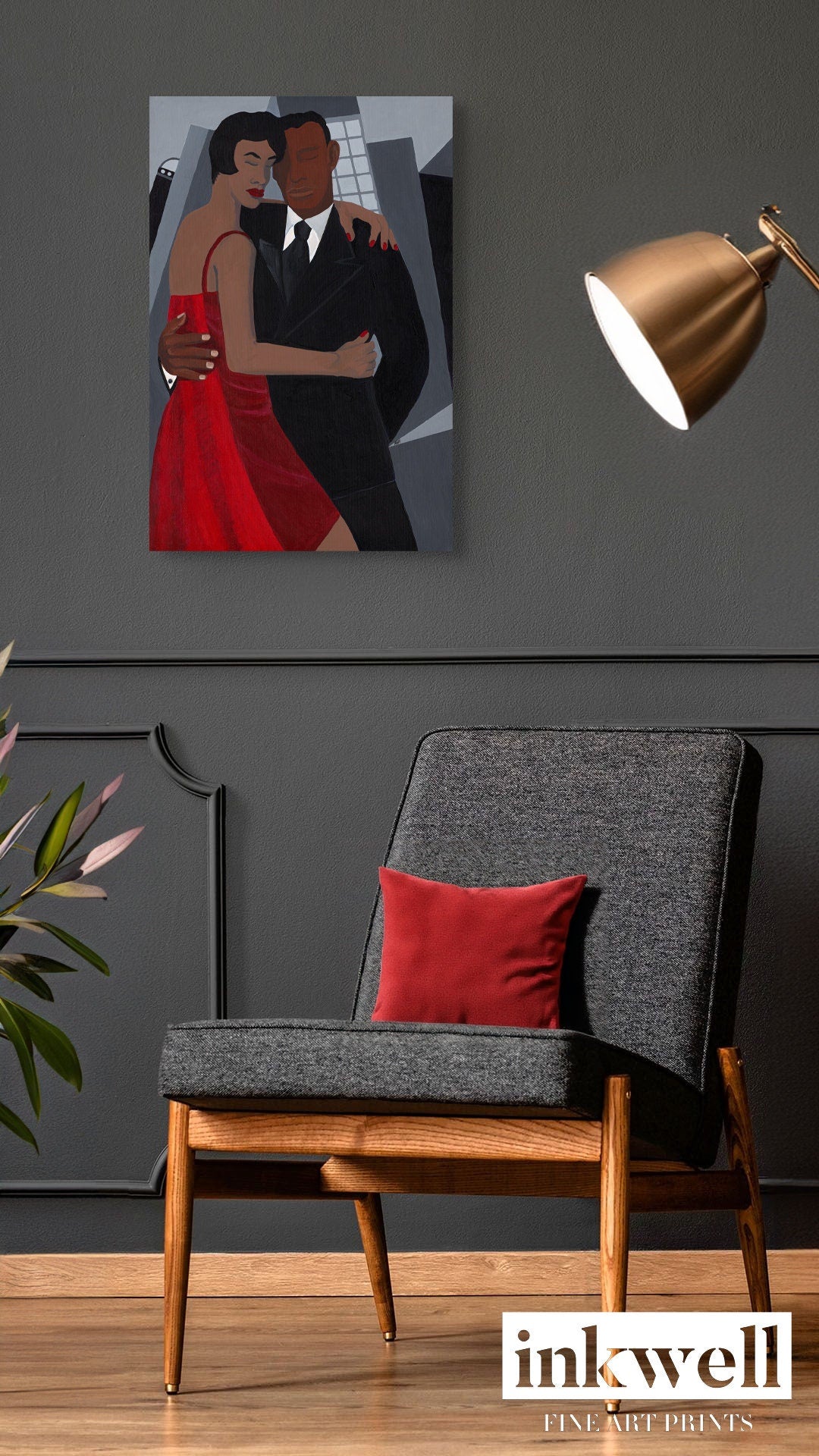 Night on the Town' art print: Elegantly dressed couple, with the woman in a red dress and the man in a black suit, embracing against a stylized urban backdrop with abstract buildings, capturing a romantic and celebratory evening atmosphere, framed in white wood. shown on gray wall above gray chair with red accent pillow