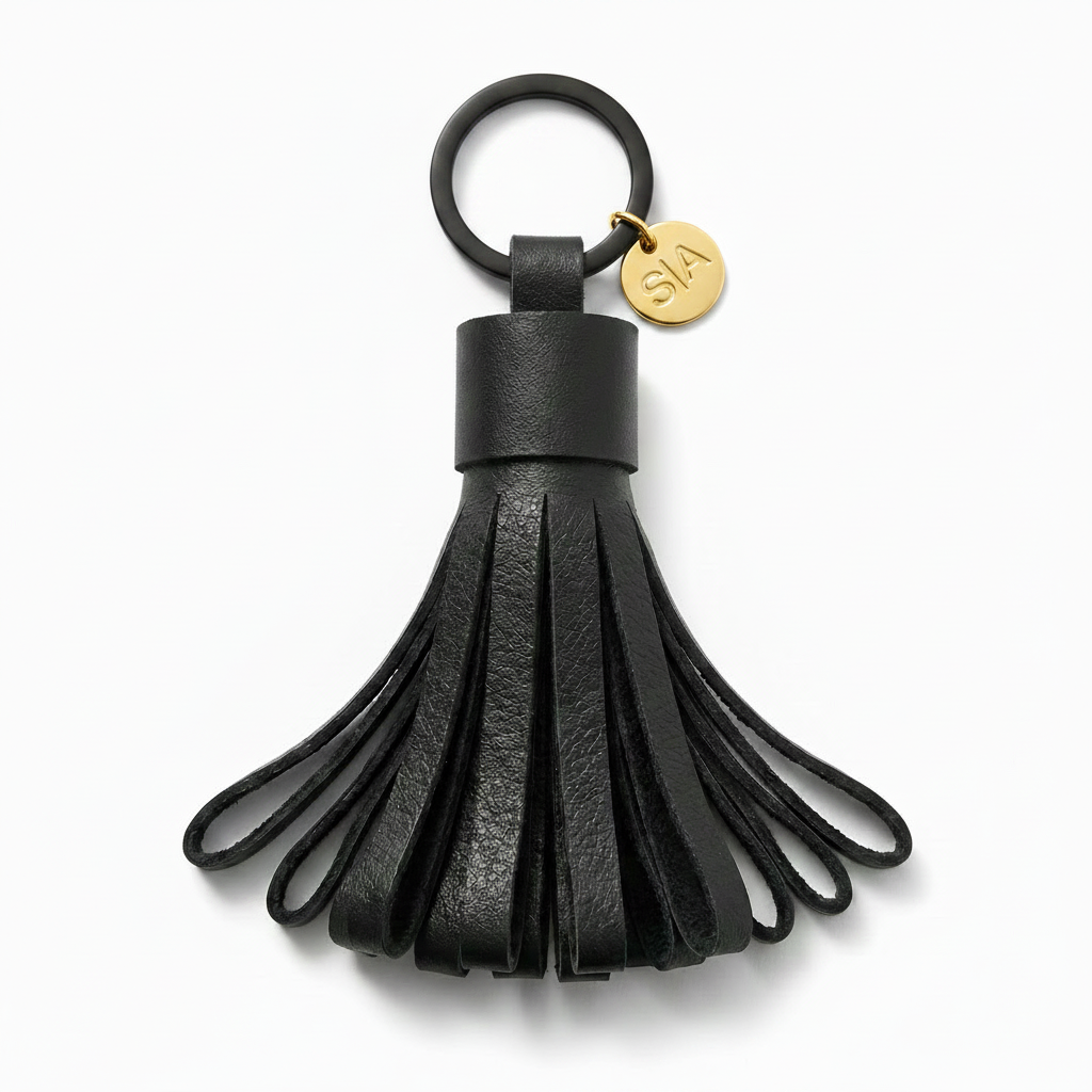 Close-up of small black leather tassel keychain with matte black ring and brass charm