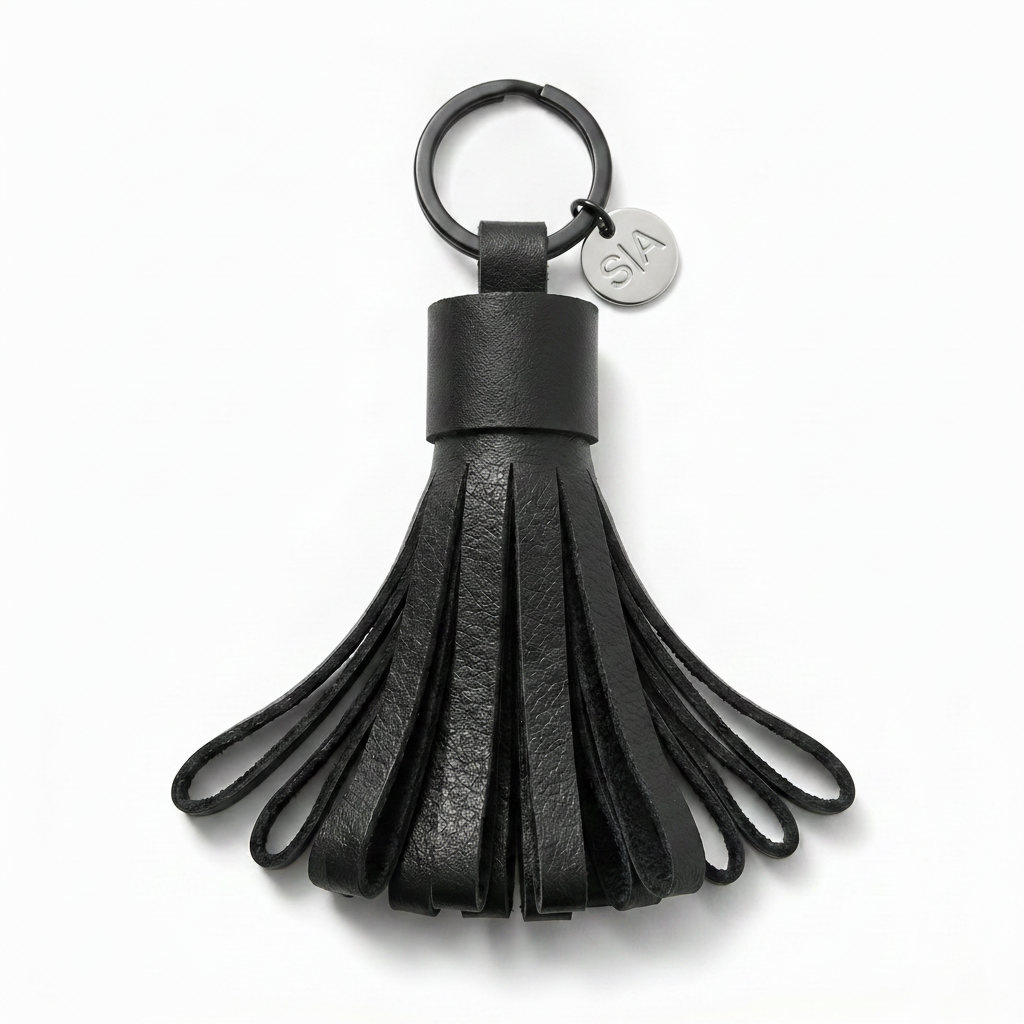 Close-up of small black leather tassel keychain with matte black ring and silver charm
