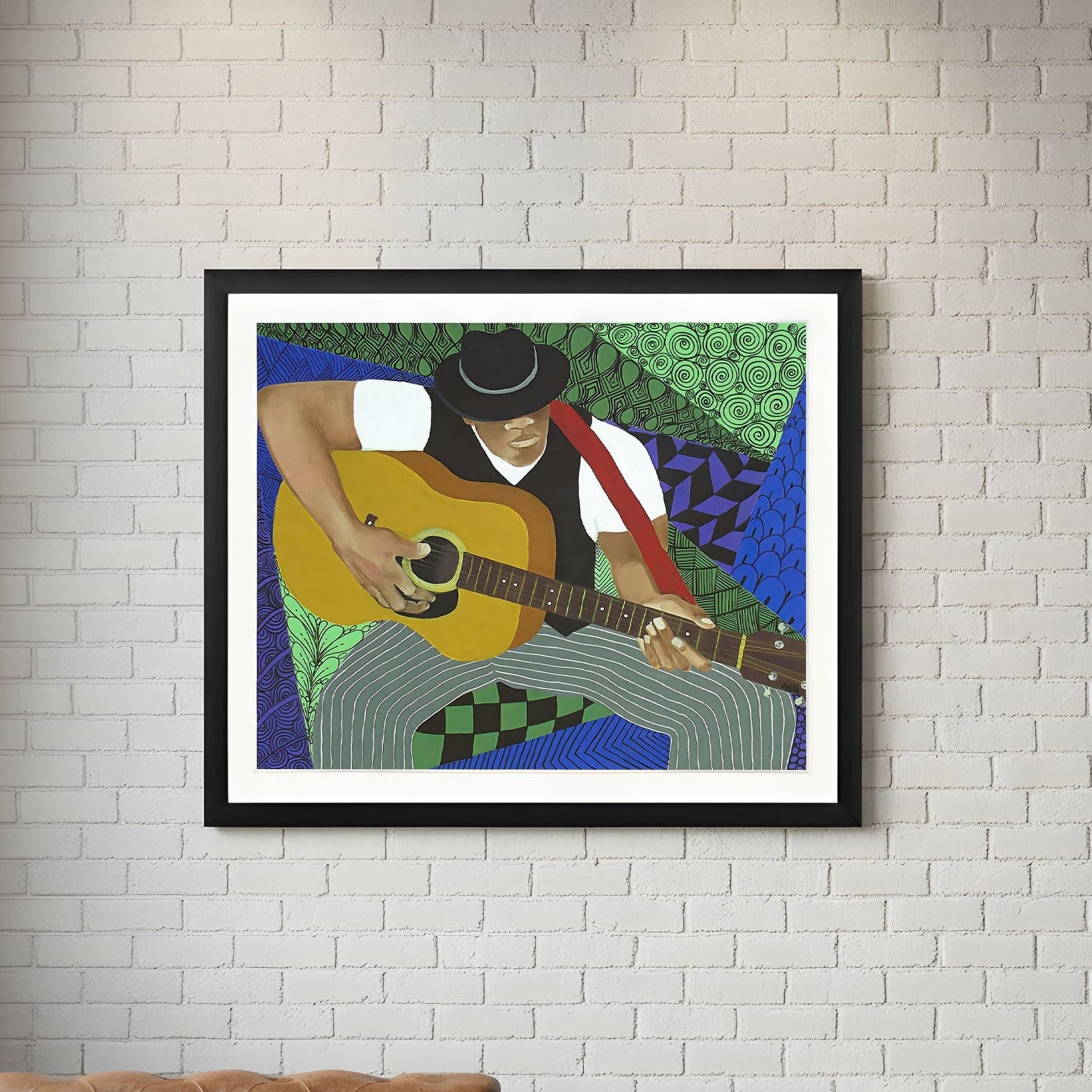 Framed artwork of a person playing guitar on a white brick wall with a brown leather sofa and wooden coffee table.