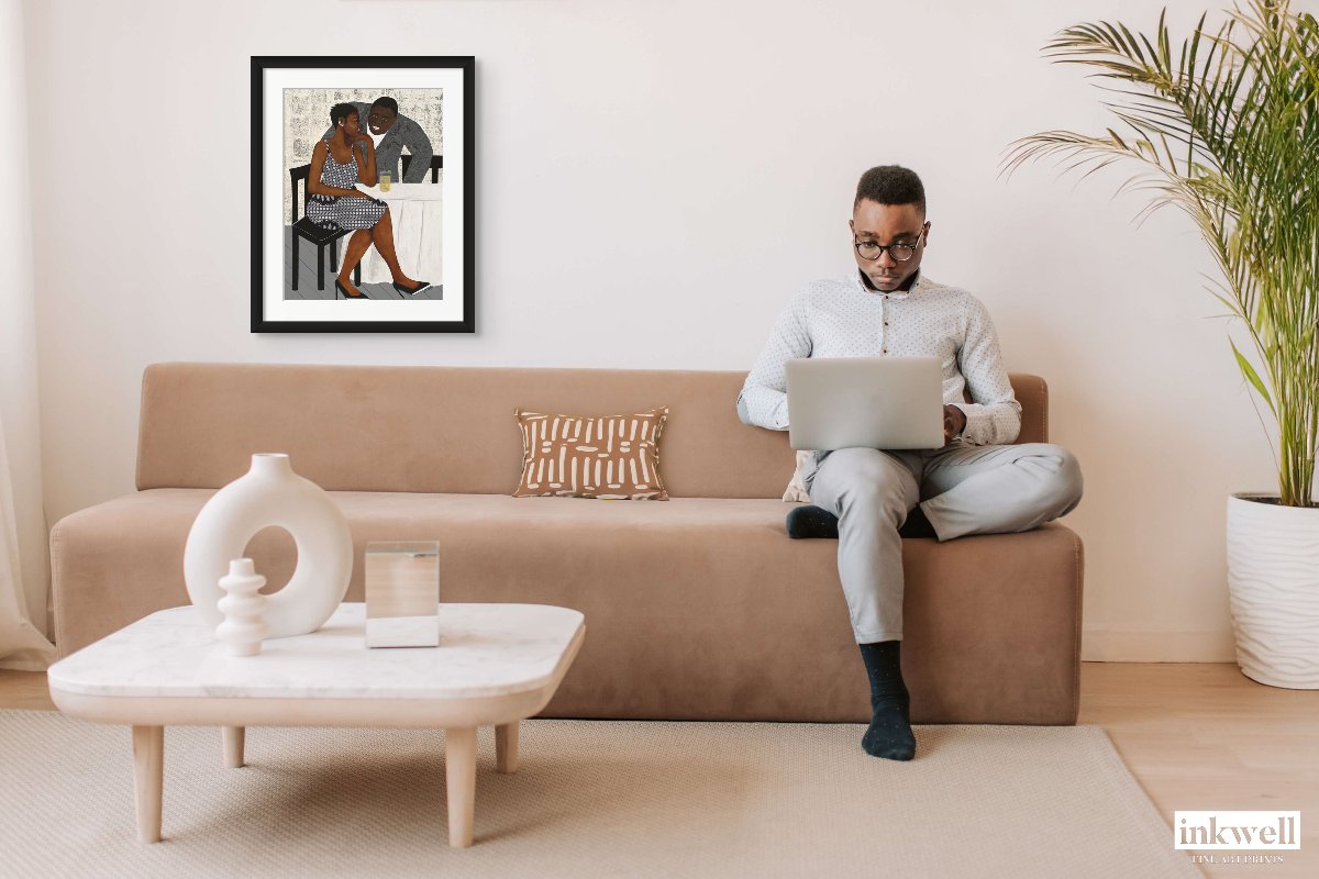 'The Conversation' paper print: African American couple immersed in dialogue, highlighted by the woman's vibrant attire and the man's relaxed posture, printed on premium fine art paper. shown above a beige sofa with a mank on a laptop